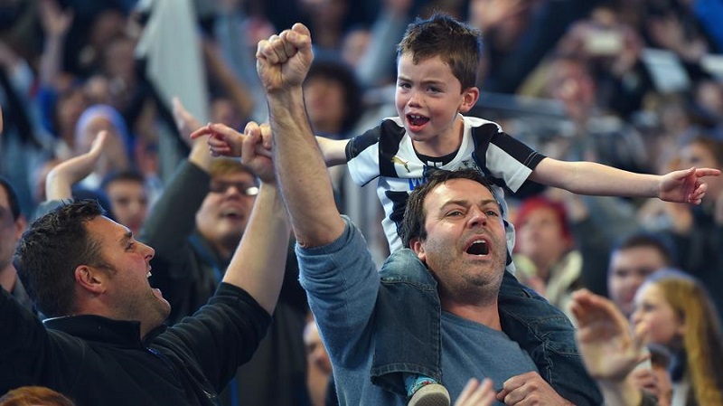 father cheers at a football game carrying his son on his shoulders