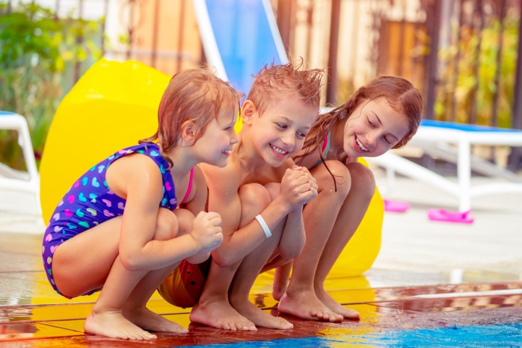 three little children crouching on the edge of a swimming pool